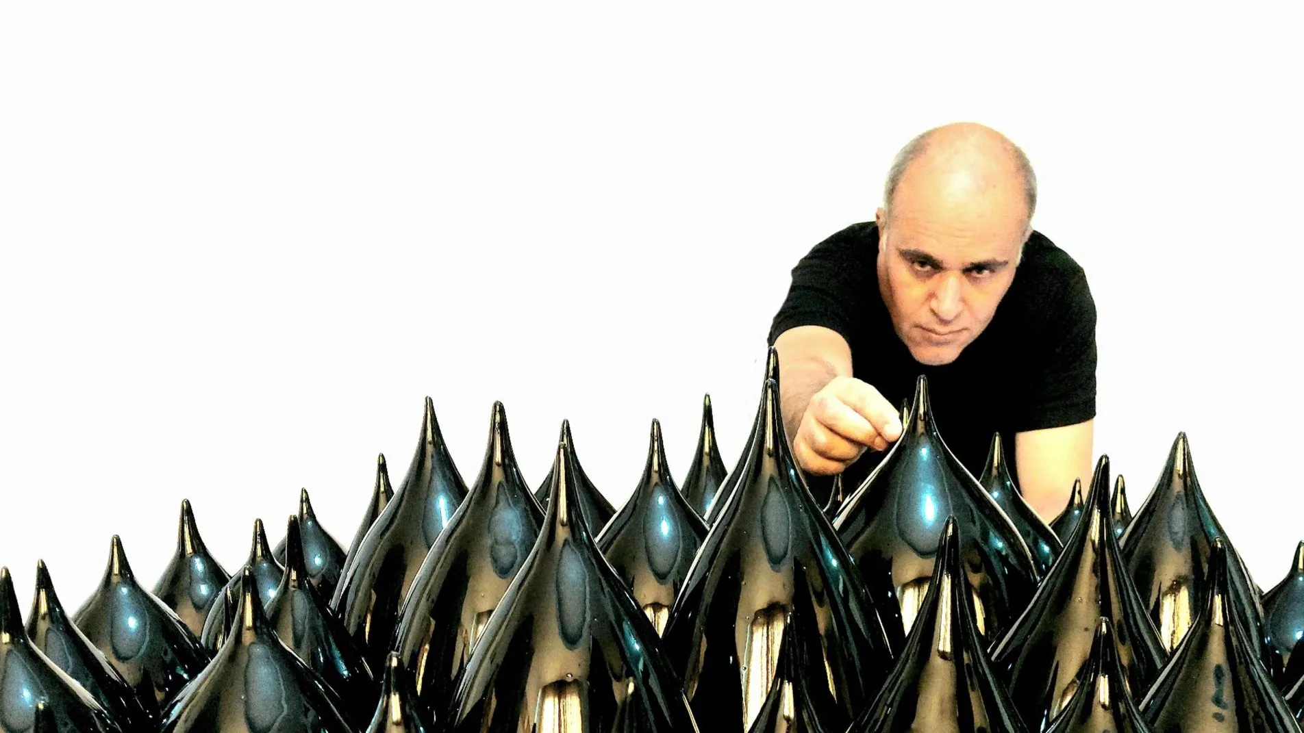 Abbas Akbari leaning over a field of black lustre cones, his hand resting on one of them